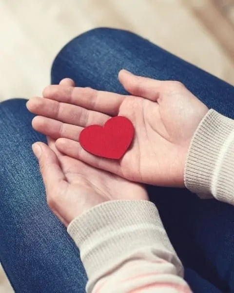 a woman holding a red paper heart in her hands