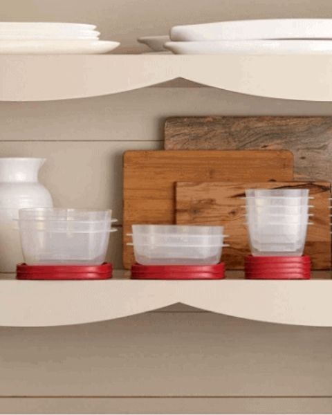 Rubbermaid containers stacked in a cupboards with a pitcher and several wooden cutting boards
