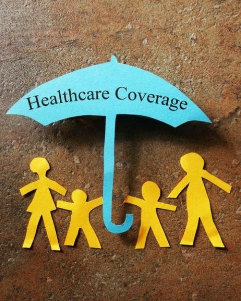 paper family under an paper umbrella with the words healthcare insurance on the umbrella