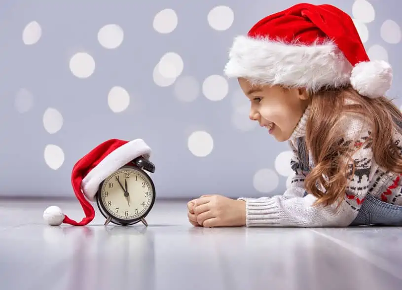Little girl in front of alarm clock while wearing a Santa hat. The Best Frugal or Free Christmas Gifts for Kids