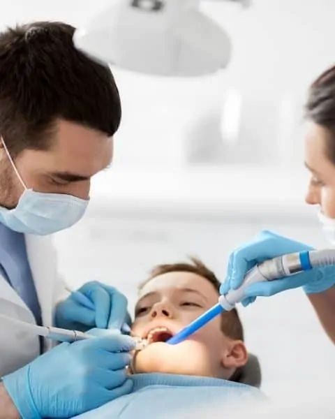 a dentist and dental hygenist performing a teeth cleaning on a child
