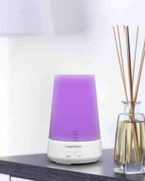 purple essential oil diffuser sitting next to some reed diffusers on a table