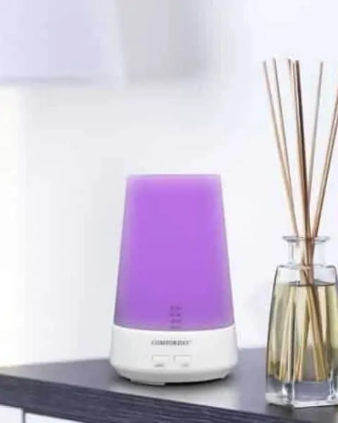 purple essential oil diffuser sitting next to some reed diffusers on a table