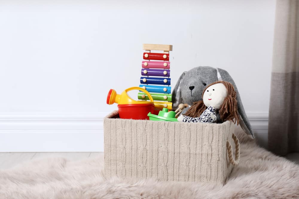 Box with different child toys on floor against white wall. Space for text