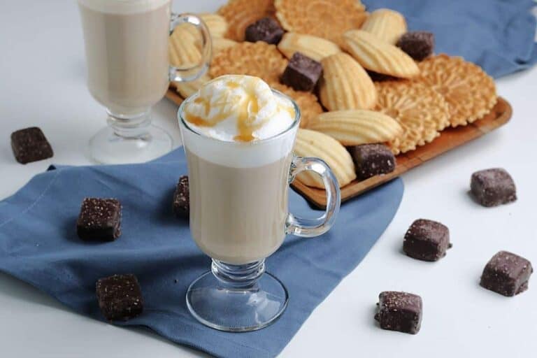 Homemade caramel vanilla latte in a cup with cookies and chocolate squares around the cup.