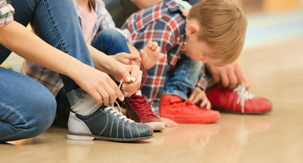 Kids putting on bowling shoes.