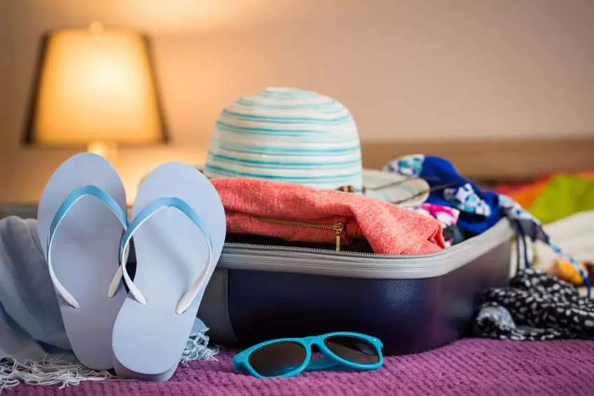 Summer hat, sandals, clothes, and sunglasses packed in a suitcase. 