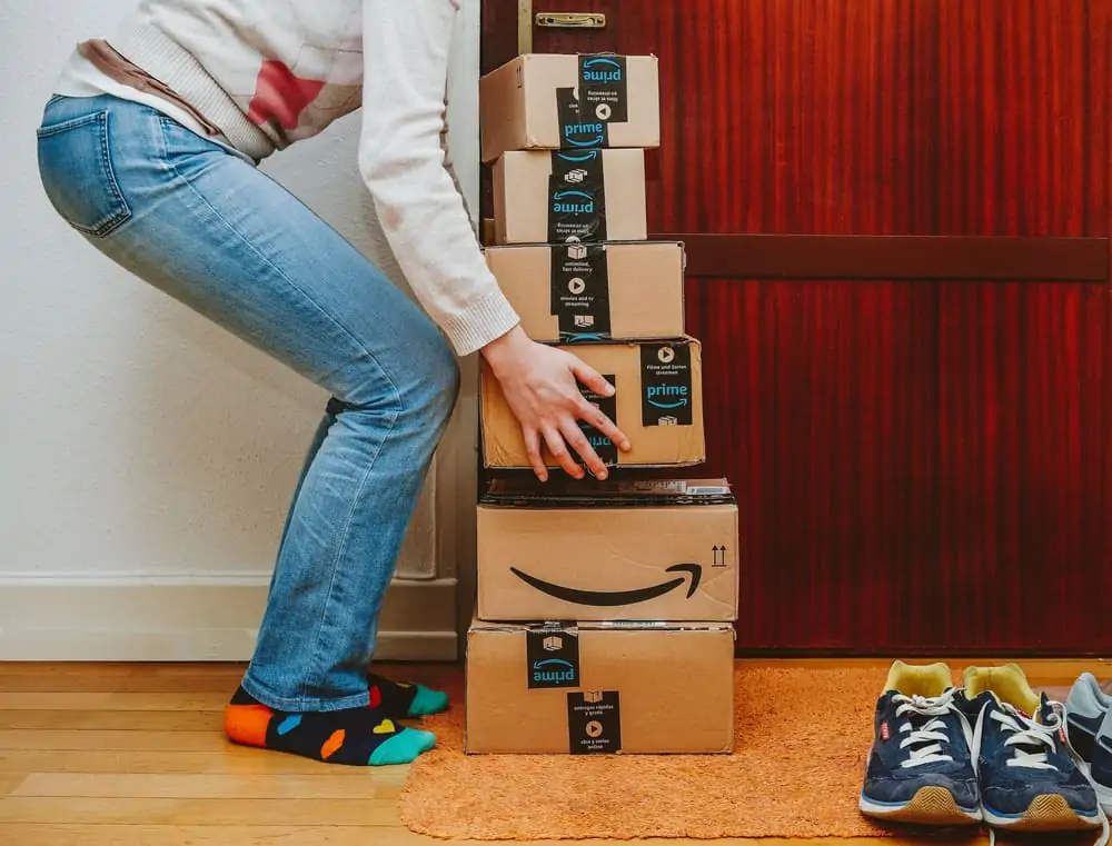 Woman lifting heavy stack of Amazon Prime packages delivered to a home door