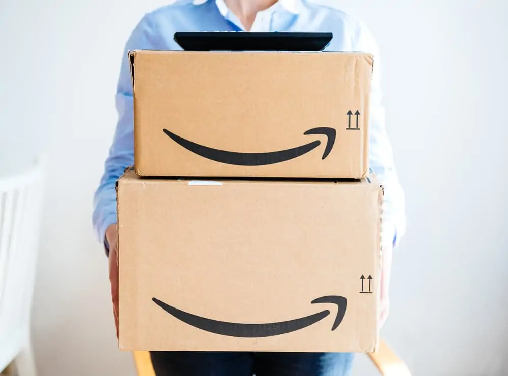 the front of happy smiling woman holding two large Amazon Prime cardboard boxing after delivery - TV set remote on top on boxes
