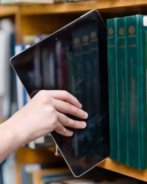 A hand pulling out a tablets from a bookshelf.