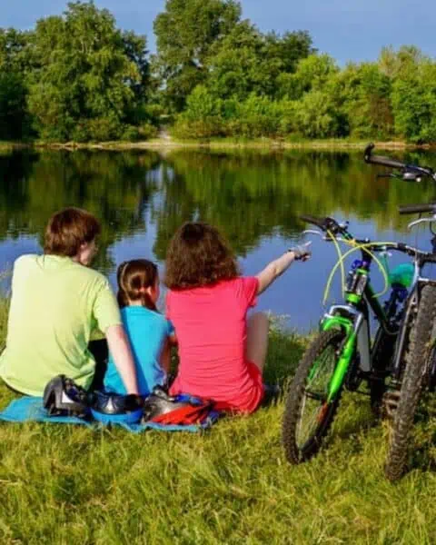 Three older children sitting by a lake with their adventure bikes.