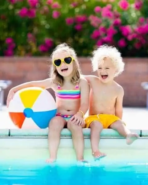 little boy and girl sitting by the pool with a beach ball