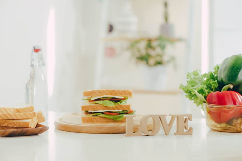 A sandwich on a plate behind a sign that reads, \"love.\"