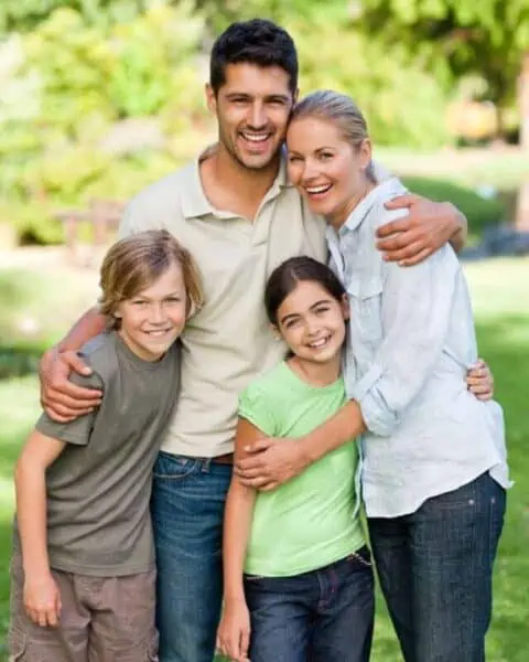 A husband and wife with their two children hugging and smiling with each other.