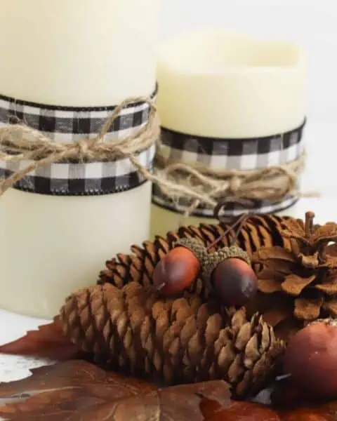 Pine cones next to leaves and candles on a table spread.