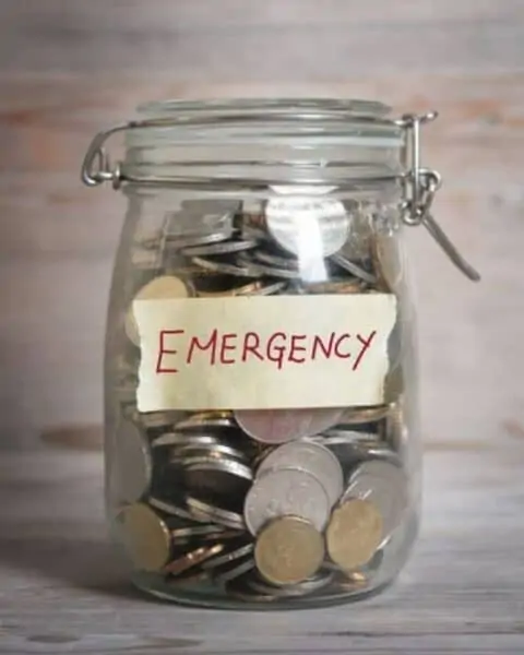 A mason jar full of coins with the label of "emergency" tapped to the jar.