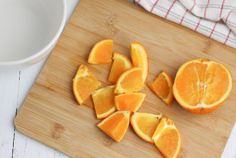 Two oranges sitting on top of a wooden cutting board, with Slow cooker and Apple