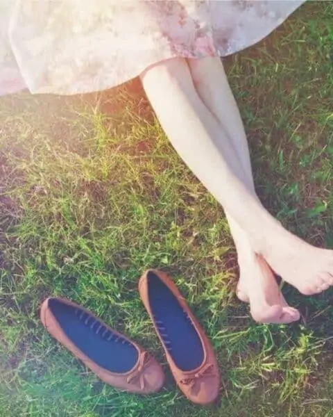 A woman sitting on a field of grass with her shoes off her feet.