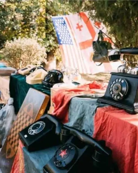 Outside flea market with antique phones, flags, board games, and other household items.