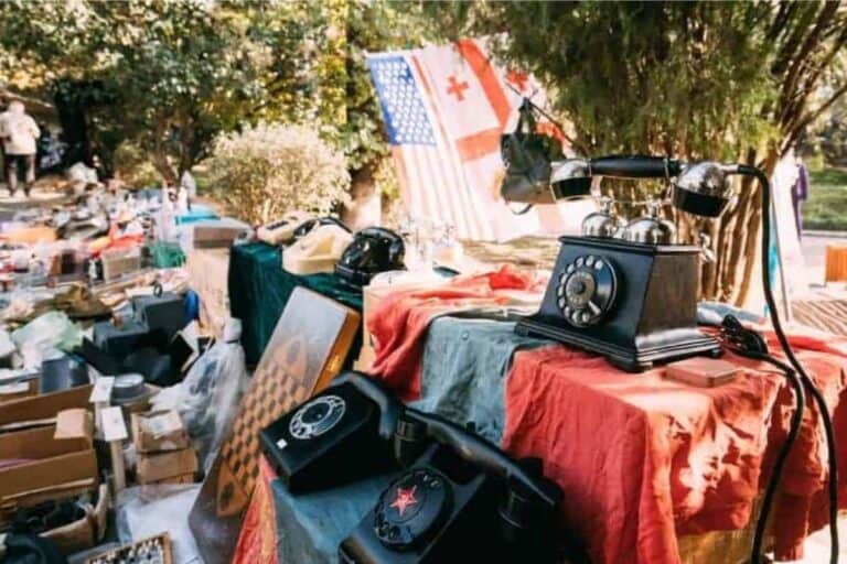 Outside flea market with antique phones, flags, board games, and other household items.