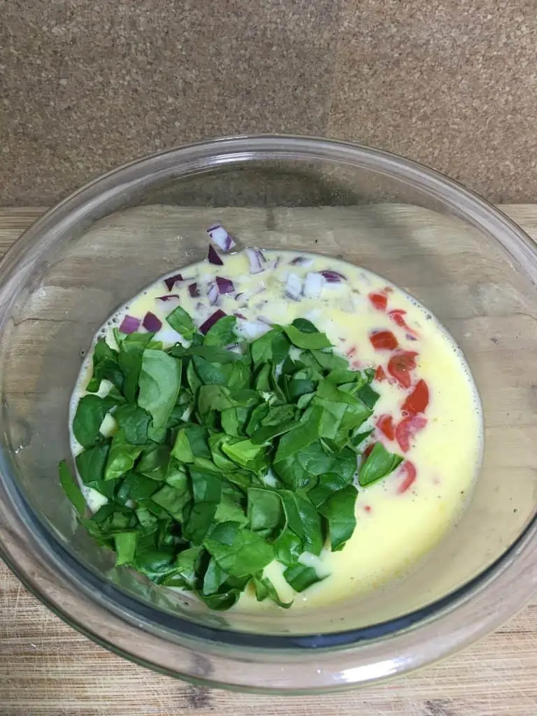 A bowl of food including eggs, milk, onions, and spinach to make a delicious egg muffin breakfast.