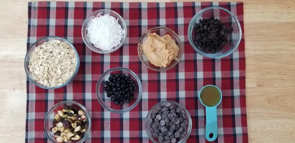 ingredients to make energy bits, chocolate chip, oats, peanut butter, coconut, raisin and nuts on a table.