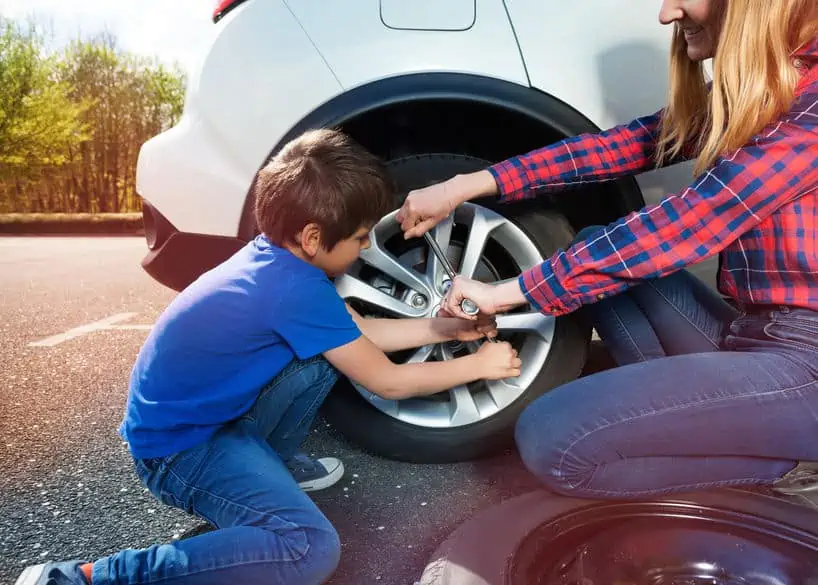Portrait of happy little boy helping his mother to change flat tyre using lug wrench outside