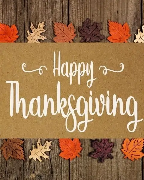 Happy Thanksgiving against a wooden background with colored leaves