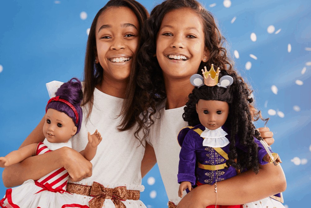 Two girls holding onto their own American Girl dolls. 