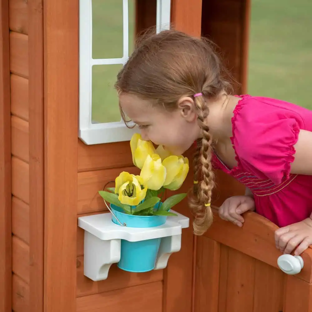 A little girl sniffing flowers from her Timberlake Cedar wooden playhouse.