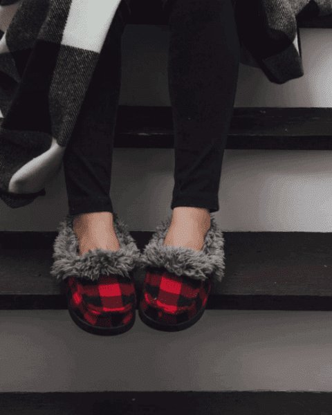 A woman sitting on the stairs wearing a pair of MUK LUKS moccasin slippers, on sale!