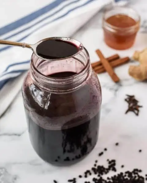 A small mouth mason jar with elderberry sauce inside and on a spoon.