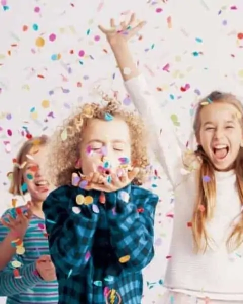 A group of girl children celebrating and blowing confetti out of their hands.