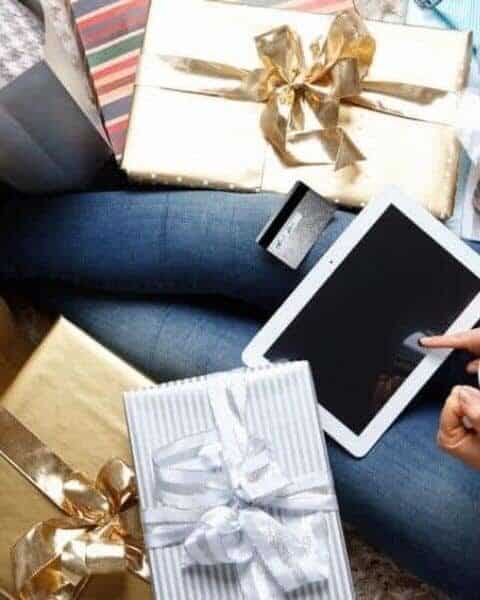 woman shopping on a tablet surrounded by wrapped gifts