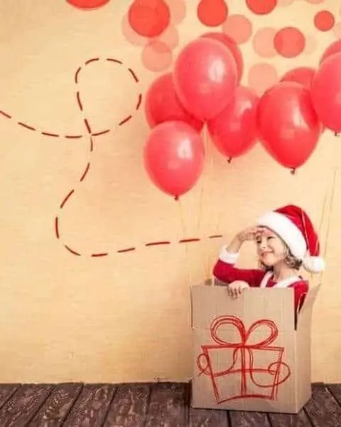 child playing in a cardboard box with balloons in the background