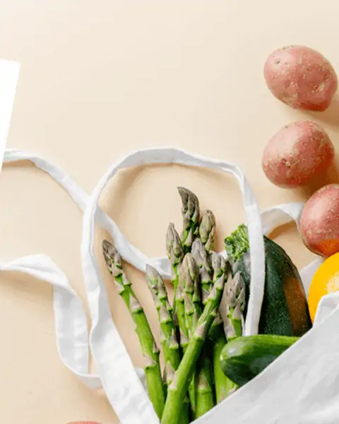 A reusable canvas grocery bag with asparagus, potatoes, and other produce inside the bag.