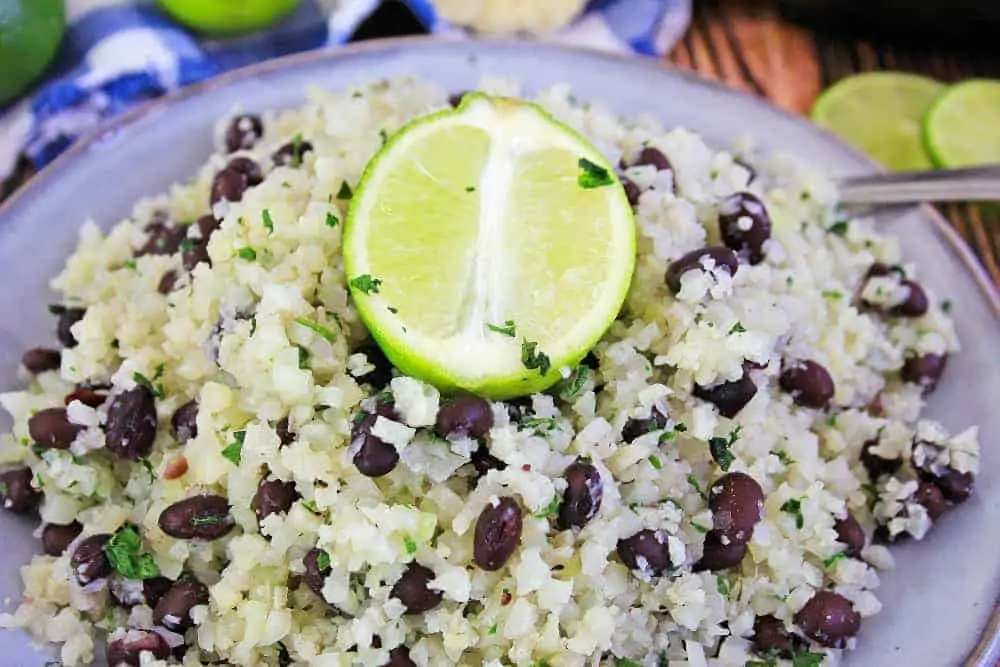 A close up of a plate of food with rice and vegetables, with Cauliflower and Lime