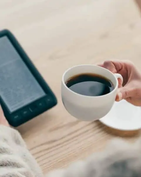 A woman drinking a cup of coffee while reading from her Kindle unlimited.