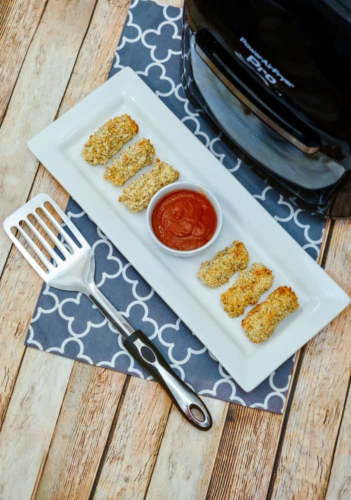 mozzarella cheese sticks on a white dish with dipping sauce, in front of an Air Fryer machine