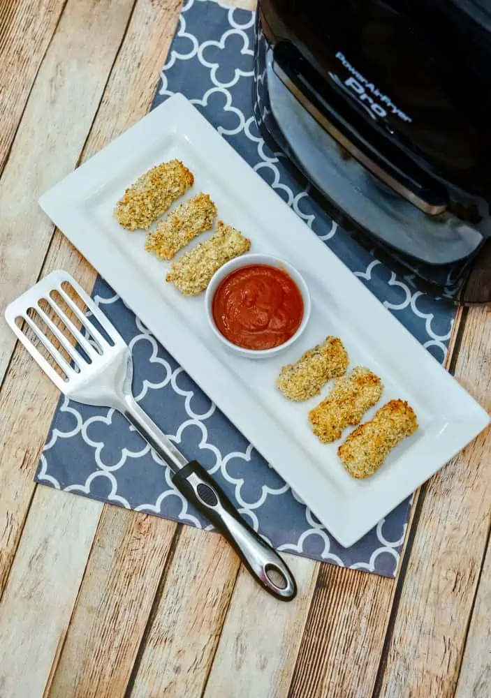 mozzarella cheese sticks on a white dish with dipping sauce, in front of an Air Fryer machine