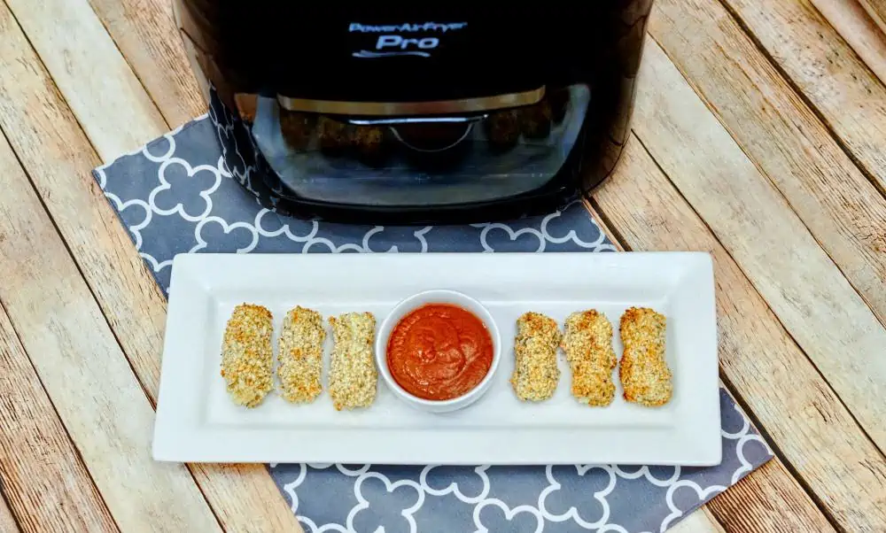 mozzarella cheese sticks on a plate with pizza sauce in front of an Air Fryer