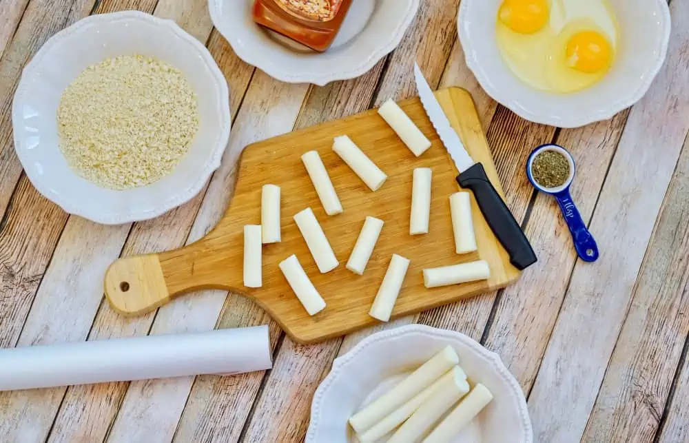 mozzarella cheese sticks cut up on a cutting board with a knife and cheese stick ingredients