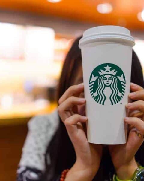 A person holding a Starbucks logo coffee cup.