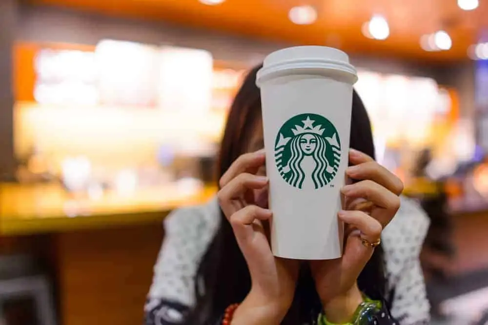 A person holding a Starbucks logo coffee cup.