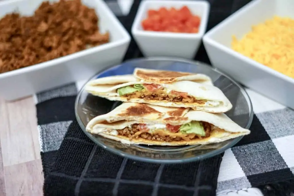 Cooked  crunch-wrap supreme on a table surrounded with toppings and garnishing.