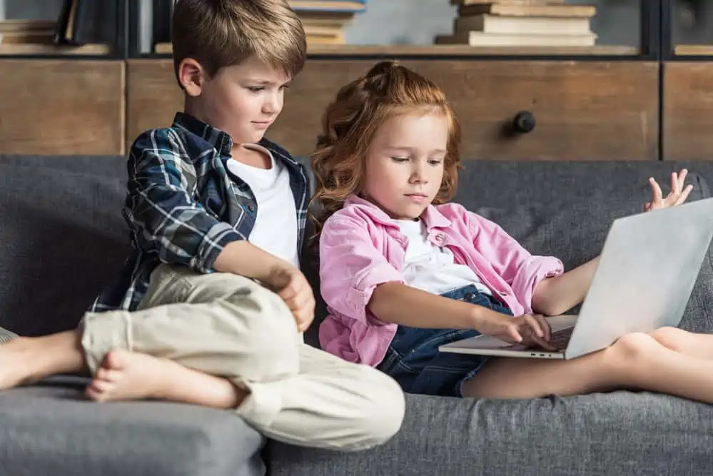 Two children sitting next to each other on the laptop to learn.