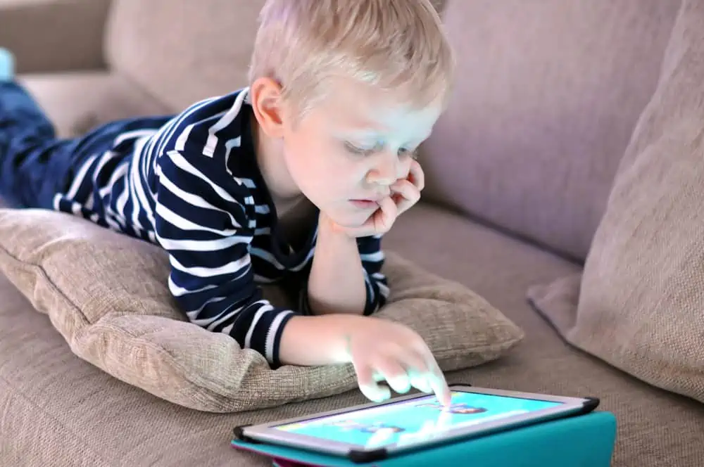 Boy reading and playing on tablet for educational purposes.
