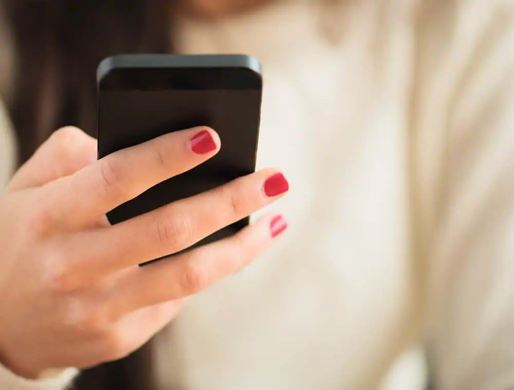 A woman holding a cell phone reviewing her iBotta app offers for cash back.