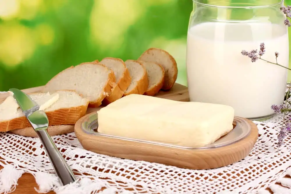 Butter on wooden holder surrounded by bread and milk on natural background