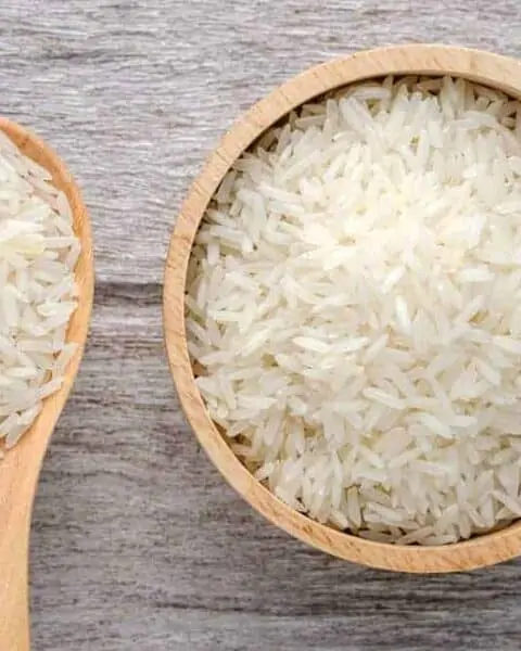 Uncooked rice in bowl on white wood background